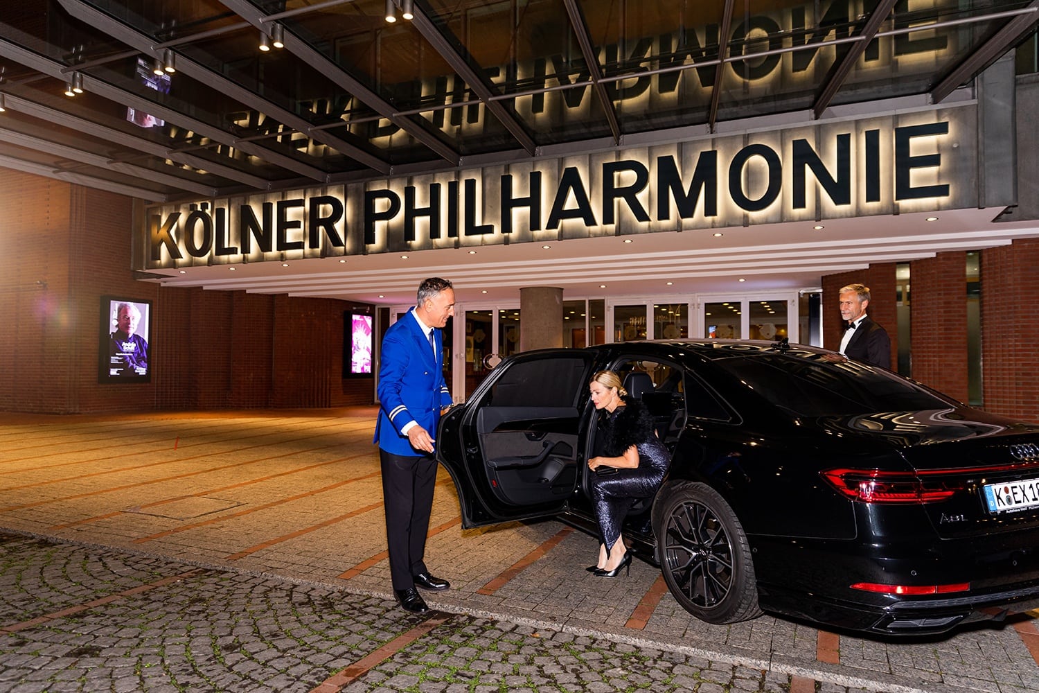 Dame im Abendkleid steigt aus einem schwarzen Auto vor der Kölner Philharmonie aus