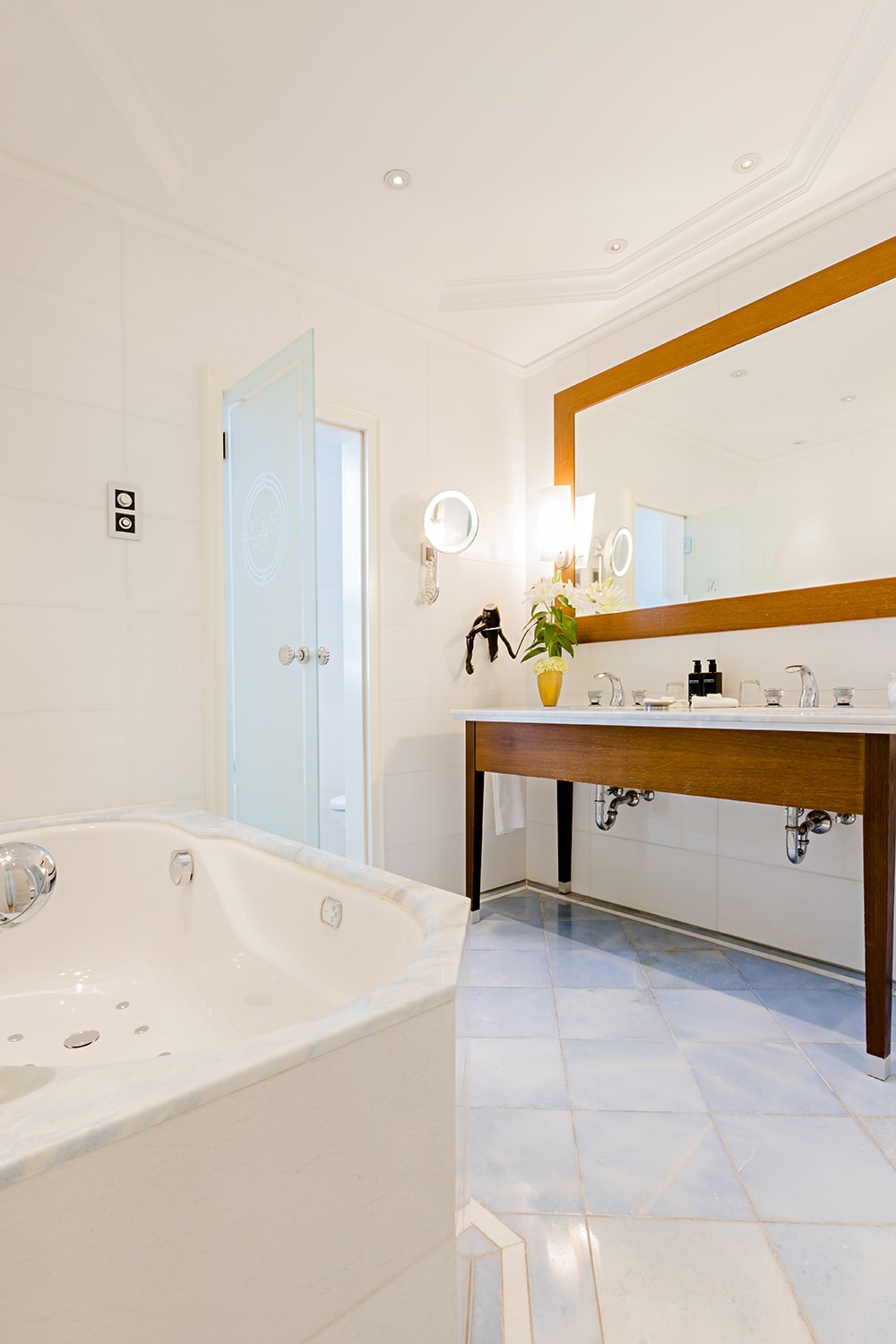 Große Badewanne steht in Badezimmer mit hellblauen Fliesen und einem Spiegel über zwei Waschbecken