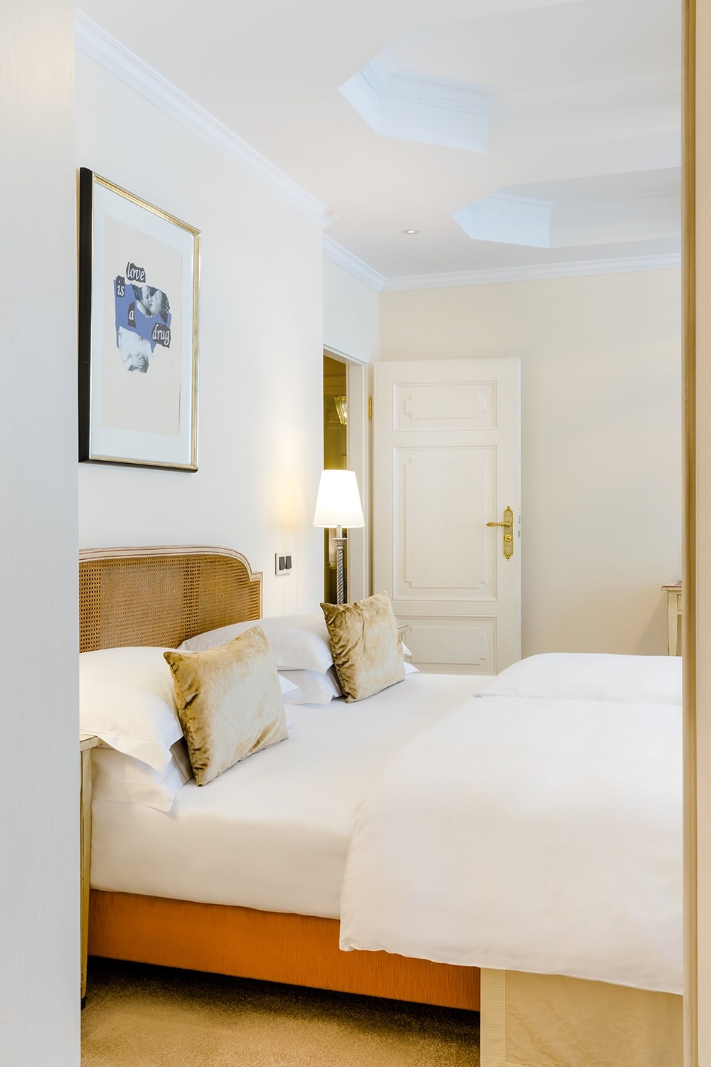 Über einem Doppelbett mit hellbraunen Zierkissen hängt ein Bild in goldenem Rahmen