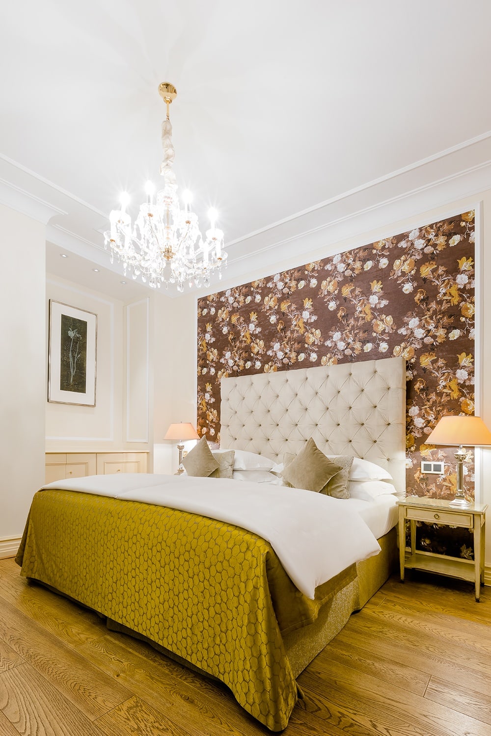 Doppelbett mit gelbem Bettüberwurf steht vor einer geblümten Wand und unter einem Kronleuchter
