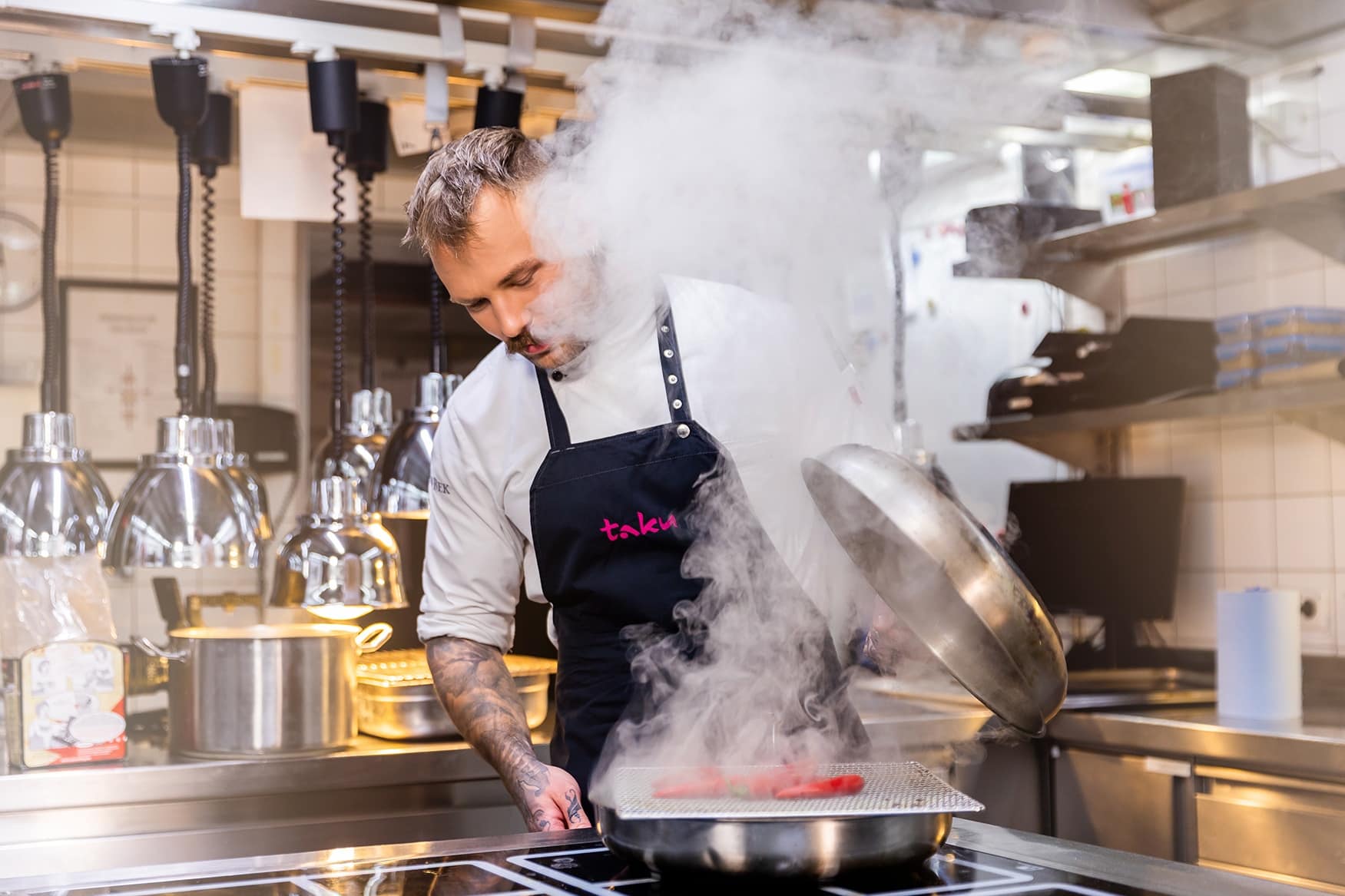 Koch hebt einen Topfdeckel in der Küche des Restaurants Köln Innenstadt an und es dampft
