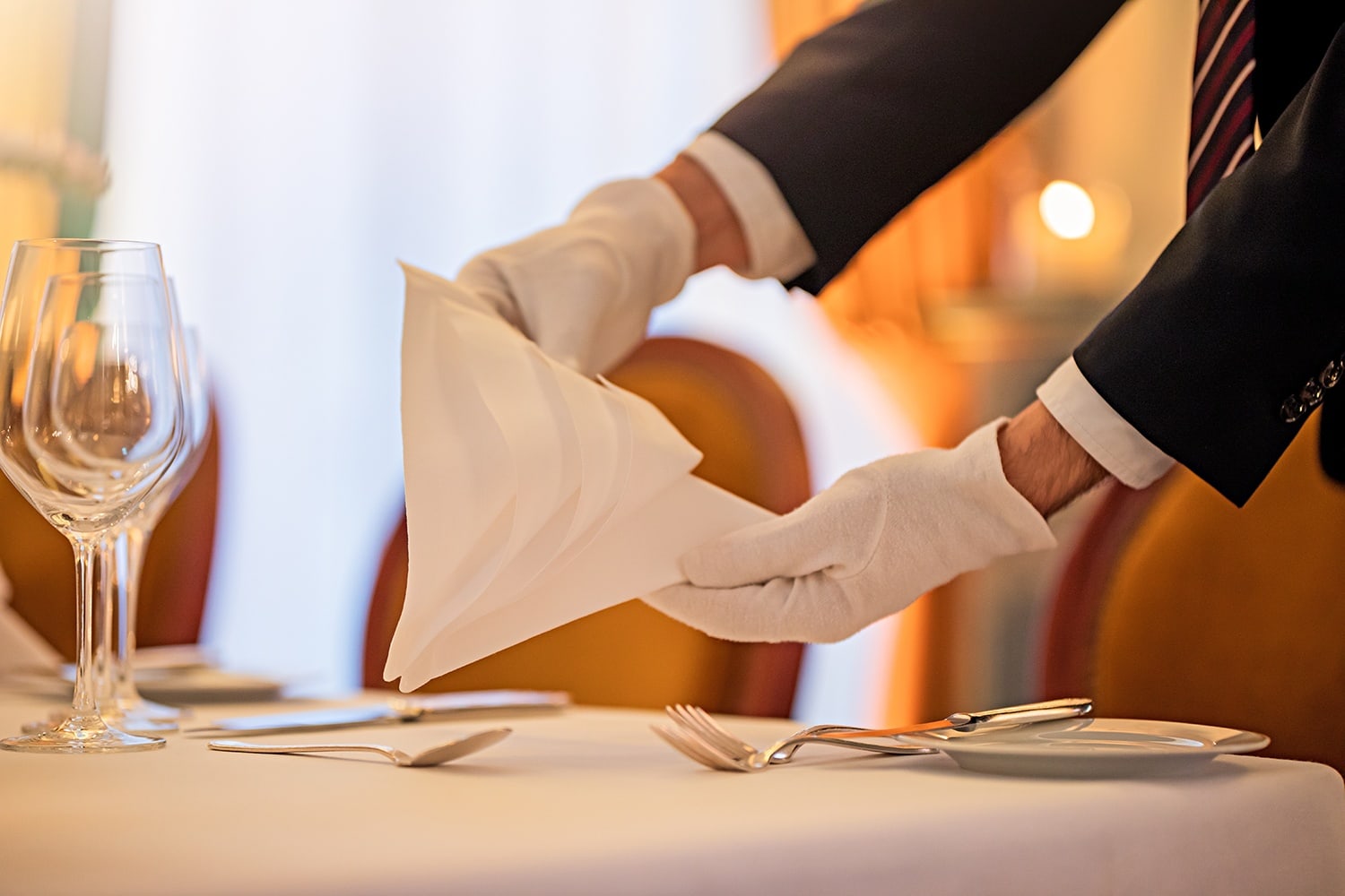 Ein Kellner deckt gerade den Tisch ein und hält in seinen Händen eine Stoffserviette