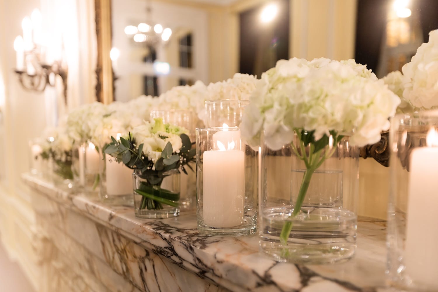 Auf einem Marmorsims stehen helle Blumen und Kerzen in einem Glas