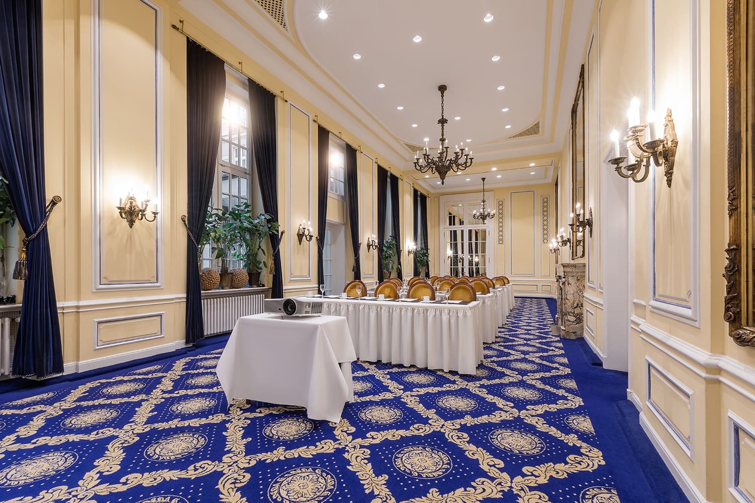 In dem länglichen Tagungsraum Köln mit blauem Teppich und Borhängen stehen kleine Tischreihen hintereinander