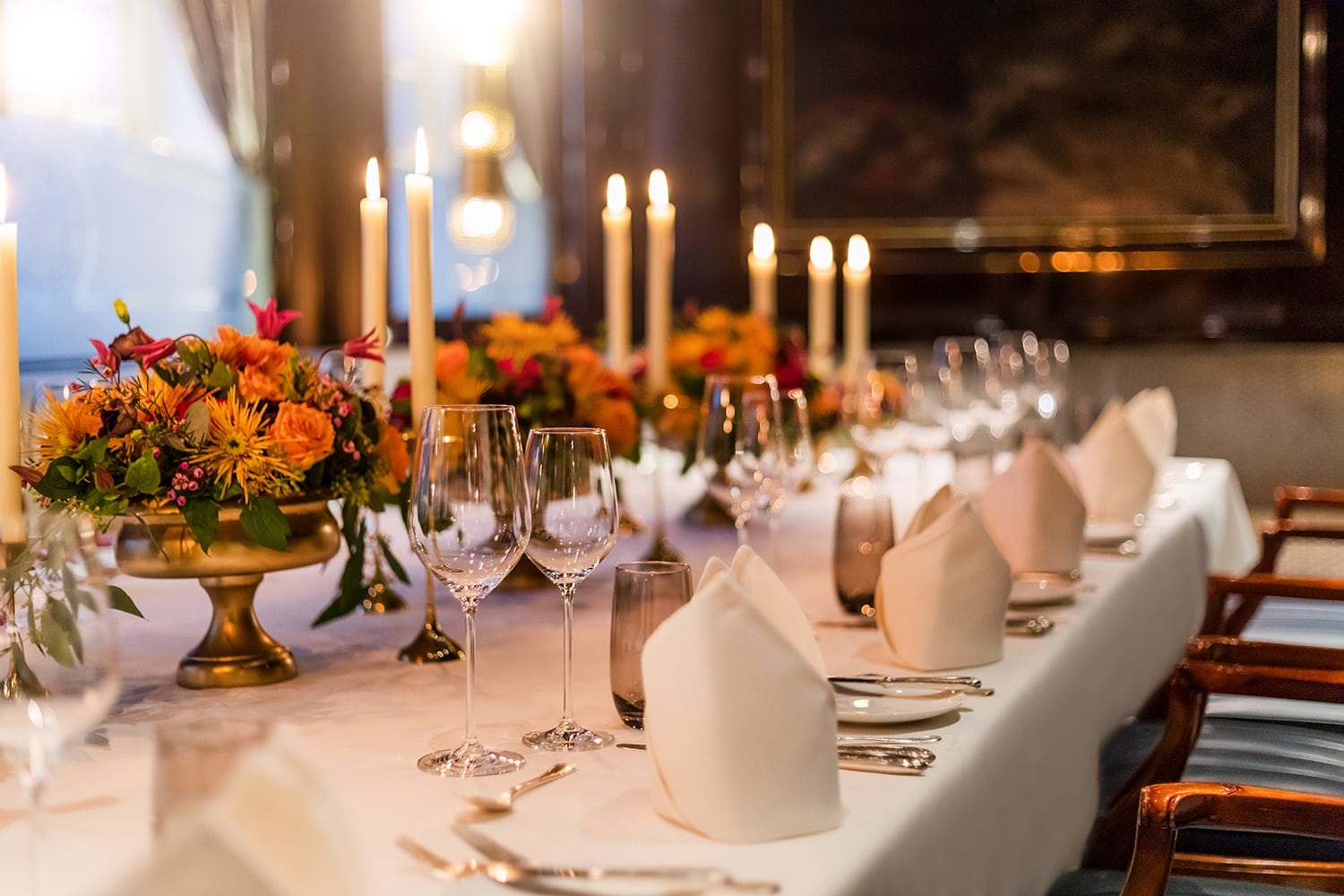 Tisch mit weißer Tischdecke und Dekoration ist mit Weingläsern, Servietten und Besteck eingedeckt