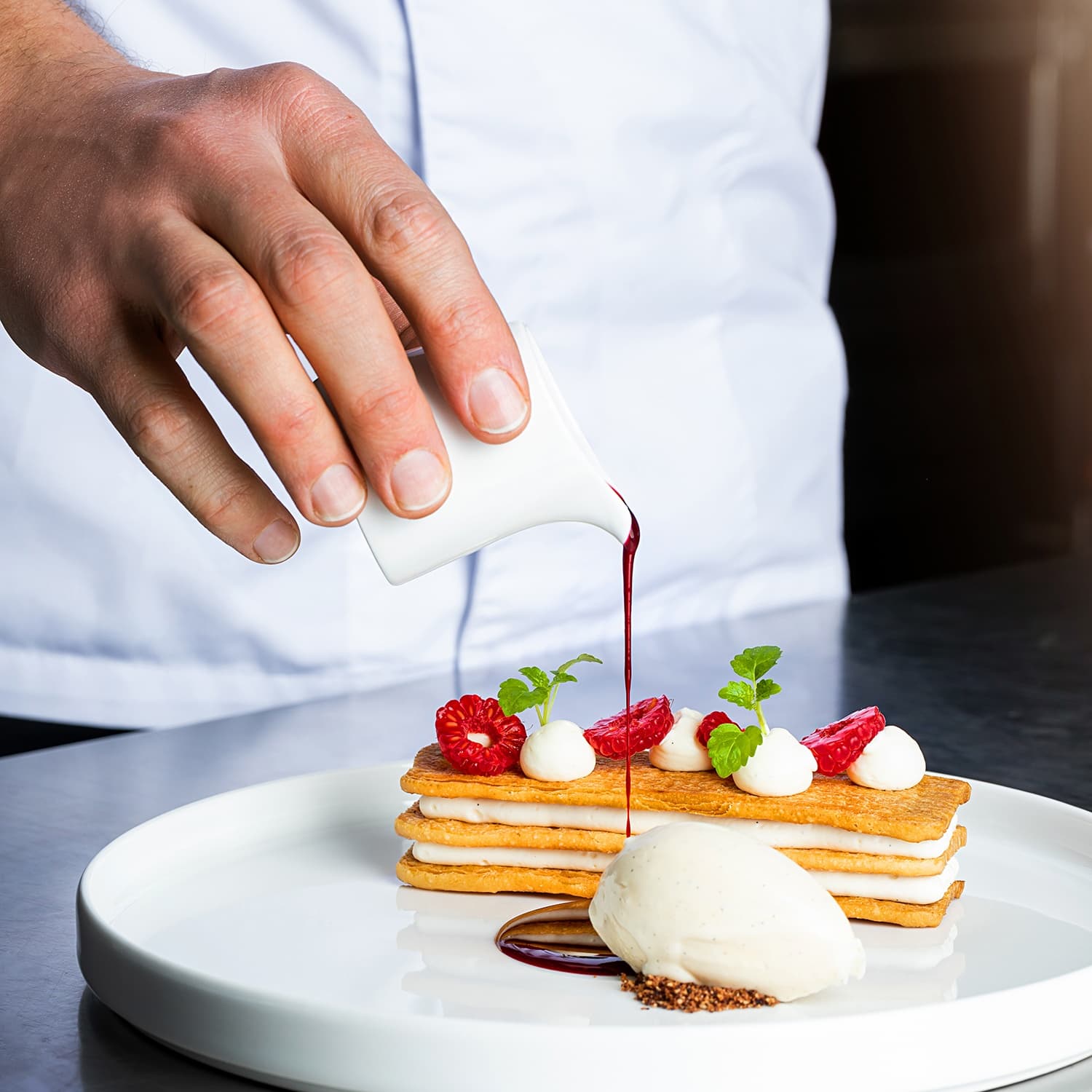 Patissier gießt Himbeersud an einem Dessert mit einer Kugel Eis im 5 Sterne Hotel Köln an