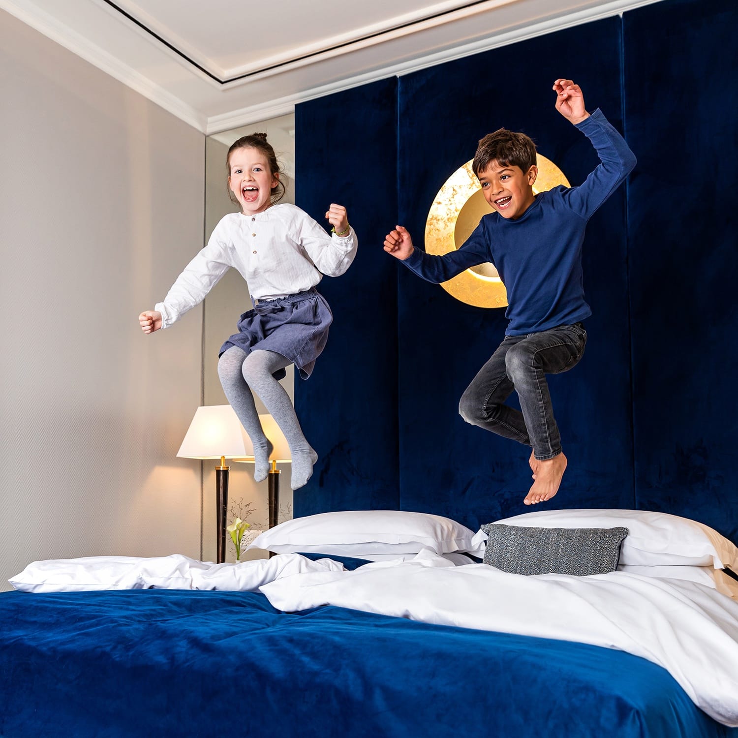 Zwei Kinder springen und toben auf einem Doppelbett im Gästezimmer im Luxushotel Köln